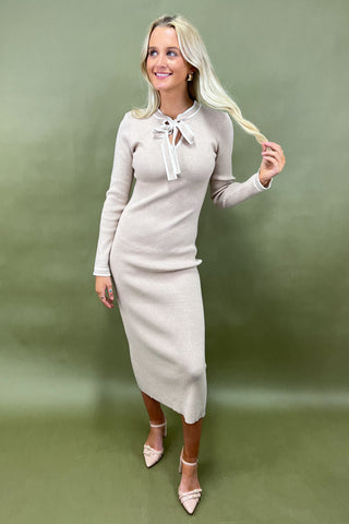 Woman wearing a beige dress with a white bow tie against a green background