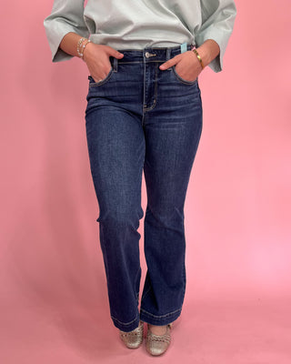 Person wearing blue jeans and a light gray shirt on a pink background