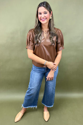 Woman wearing a brown top and blue jeans against a green background