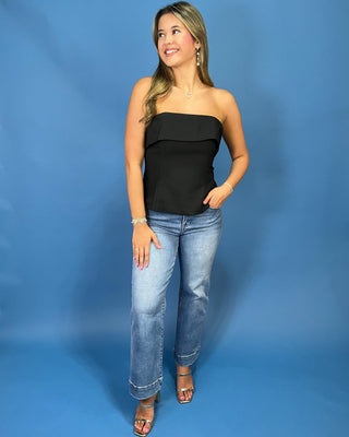 A woman modeling a black strapless ruffle-trimmed top with light-wash blue jeans and metallic sandal