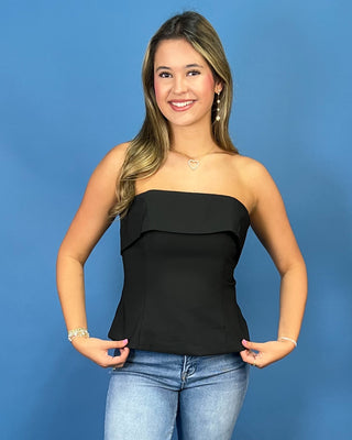 A woman modeling a black strapless ruffle-trimmed top with blue jean