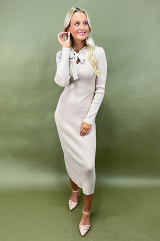 Woman wearing a light gray dress with a bow detail on a green background