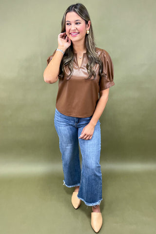 Woman wearing a brown blouse and blue jeans against a green background