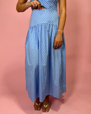 Person wearing a blue polka dot dress against a pink background