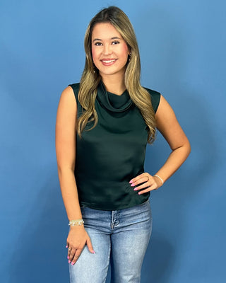 A woman with blonde hair wearing a dark green satin sleeveless top and light blue jeans
