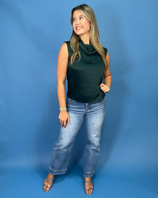 A woman modeling a dark forest green sleeveless cowl-neck top with light-wash blue jean
