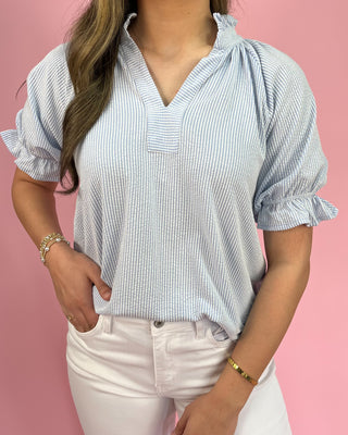 Woman wearing a blue and white striped blouse with ruffled sleeves against a pink background