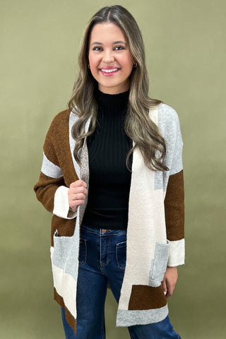 Woman wearing a brown, white, and blue cardigan against a green background