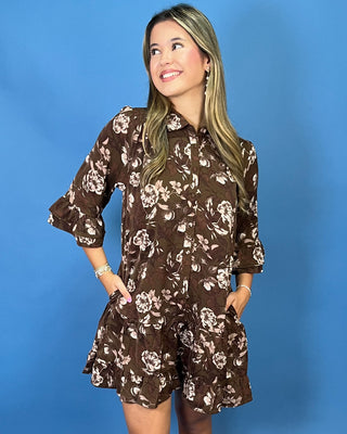 A woman modeling a brown short-sleeve floral romper with beige and white flower
