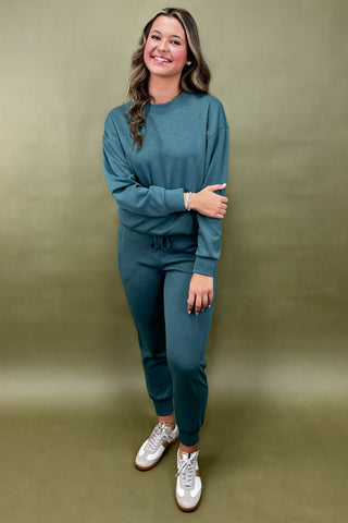Woman wearing a teal outfit with white sneakers against a green background