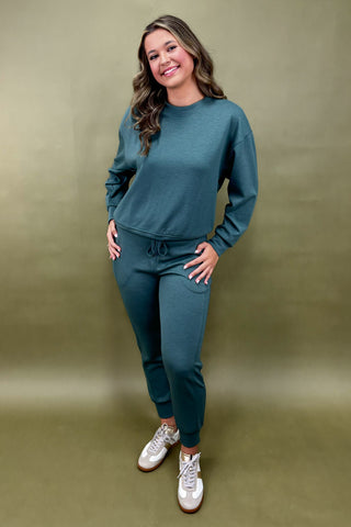 Woman wearing a teal outfit with white sneakers against a green background