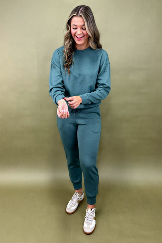 Woman wearing a teal outfit with white sneakers against a green background