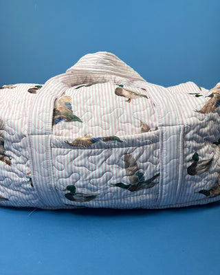 Ida Mae Home quilted duck print duffle bag with striped fabric, padded handles, spacious zip-top compartment, available in pink or blue.