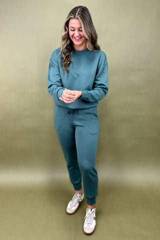 Woman wearing a teal outfit with white sneakers on a beige background