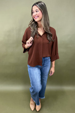 Woman wearing a brown blouse and blue jeans against a green background