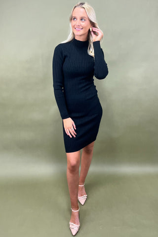 Woman wearing a black ribbed dress against a green background