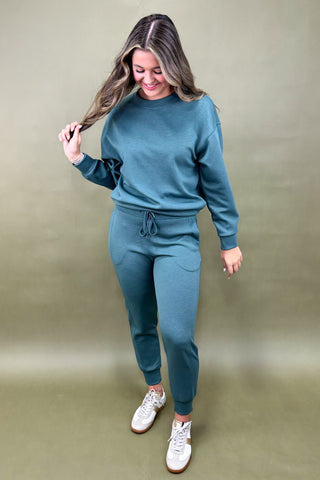 Woman wearing a teal outfit with white sneakers against a green background