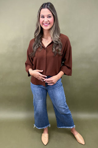Woman wearing a brown blouse and blue jeans against a green background
