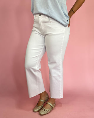 Person wearing white jeans and gold flats on a pink background