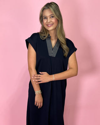 Woman wearing a navy dress with a white collar against a pink background
