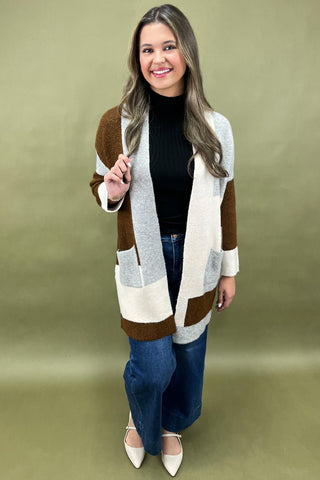 Woman wearing a striped cardigan over a black top and blue jeans on a green background