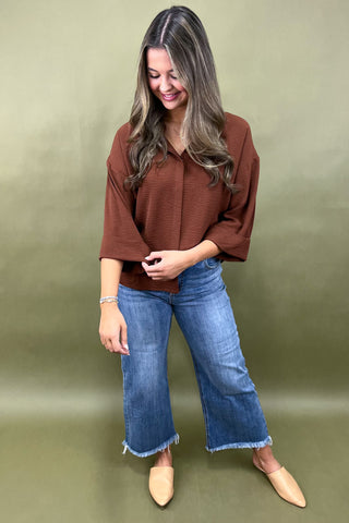 Woman wearing a brown blouse and blue jeans against a green background