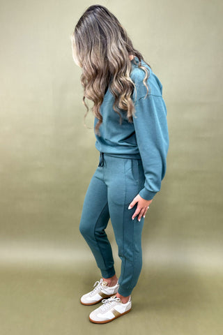 Person wearing a teal tracksuit with white sneakers on a beige background