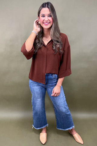 Woman wearing a brown blouse and blue jeans against a green background