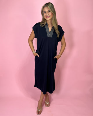 Woman wearing a navy dress with a striped shirt underneath on a pink background