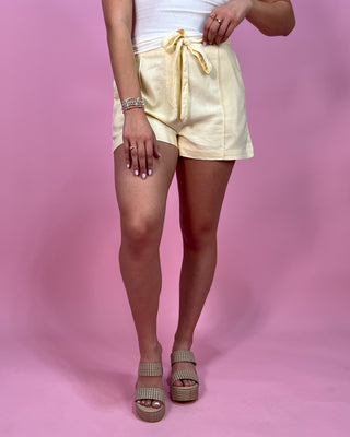 Person wearing light yellow shorts on a pink background