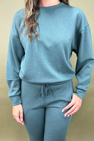 Woman wearing a teal outfit with white sneakers against a green background
