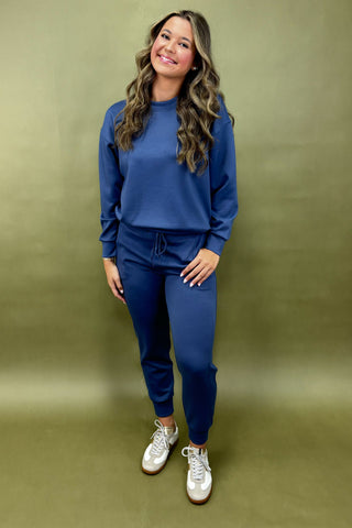 Woman wearing a blue outfit with white sneakers against a green background