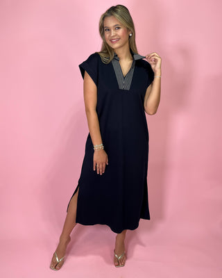 Woman wearing a navy dress with a striped shirt underneath on a pink background