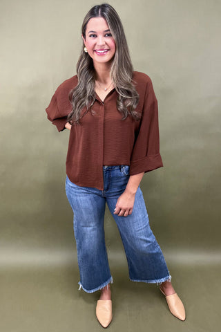 Woman wearing a brown blouse and blue jeans against a green background