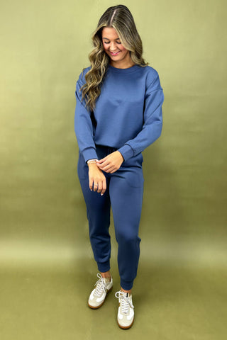 Woman wearing a blue outfit with white sneakers against a green background