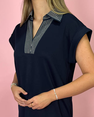 Navy blue top with striped collar worn by a person on a pink background