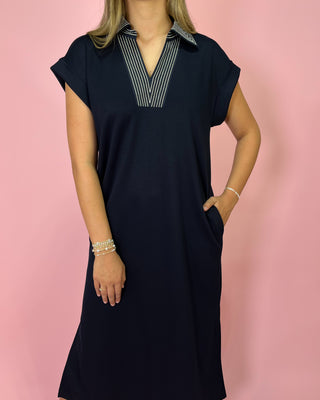 Woman wearing a navy dress with a striped collar against a pink background