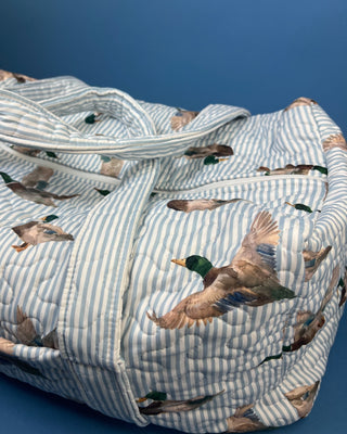 Ida Mae Home quilted duck print duffle bag with striped fabric, padded handles, spacious zip-top compartment, available in pink or blue.
