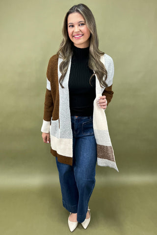 Woman wearing a long, patterned cardigan over a black top and blue jeans on a green background