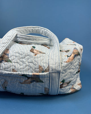 Ida Mae Home quilted duck print duffle bag with striped fabric, padded handles, spacious zip-top compartment, available in pink or blue.