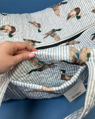 Ida Mae Home quilted duck print duffle bag with striped fabric, padded handles, spacious zip-top compartment, available in pink or blue.
