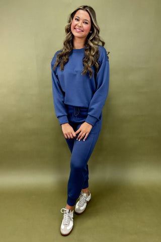 Woman wearing a blue outfit with white sneakers against a green background