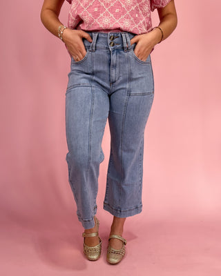 Person wearing blue jeans and a pink top against a pink background