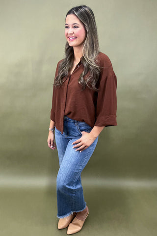 Woman wearing a brown blouse and blue jeans against a green background