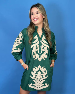 A woman modeling a green short-sleeve tunic dress with cream-colored embroidered patterns