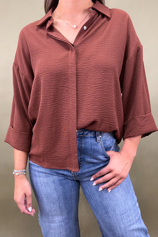 Person wearing a brown button-up shirt and blue jeans against a neutral background