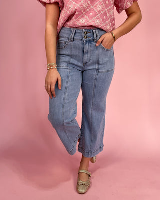 Person wearing blue jeans and a pink patterned top on a pink background