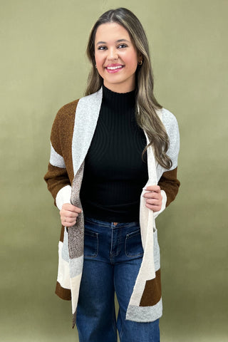 Woman wearing a brown and white cardigan over a black top and blue jeans on a green background