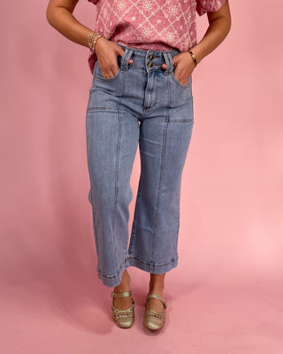 Person wearing pink patterned top and blue jeans on a pink background