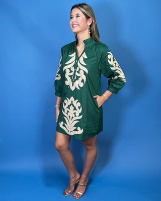 A woman modeling a green short-sleeve tunic dress with cream-colored embroidered patterns
